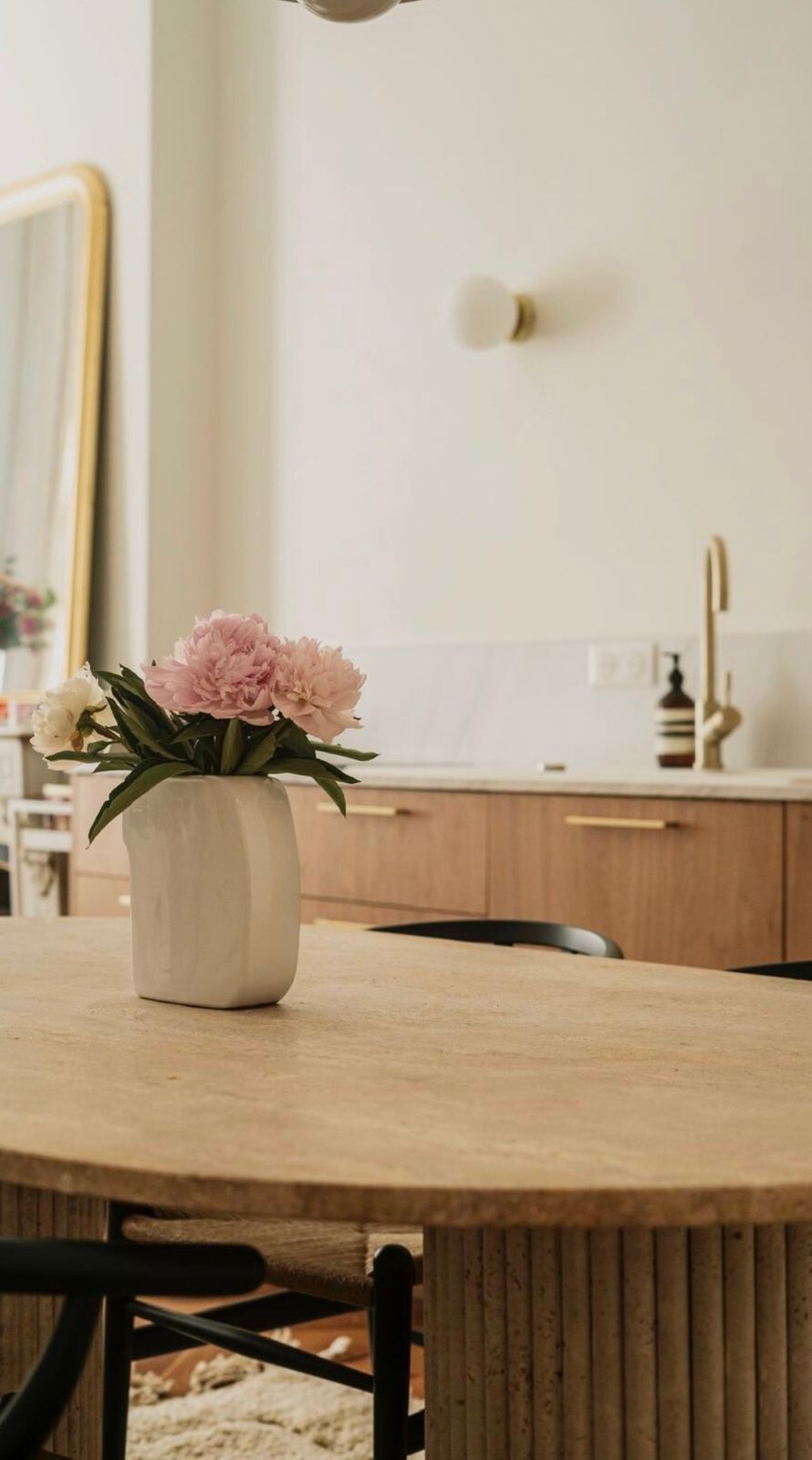 Pivoines dans un vase blanc sur une table en travertin, cuisine en bois et laiton