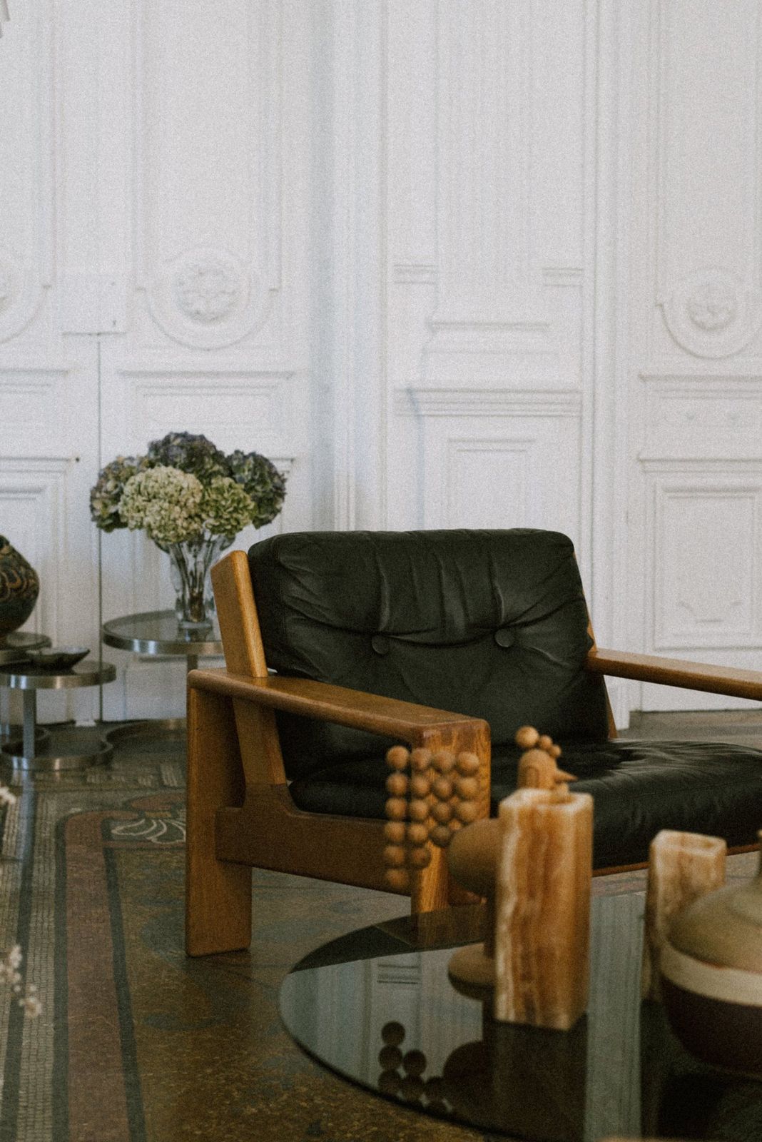 Fauteuil en bois et cuir noir devant des boiseries blanches, hortensias séchés