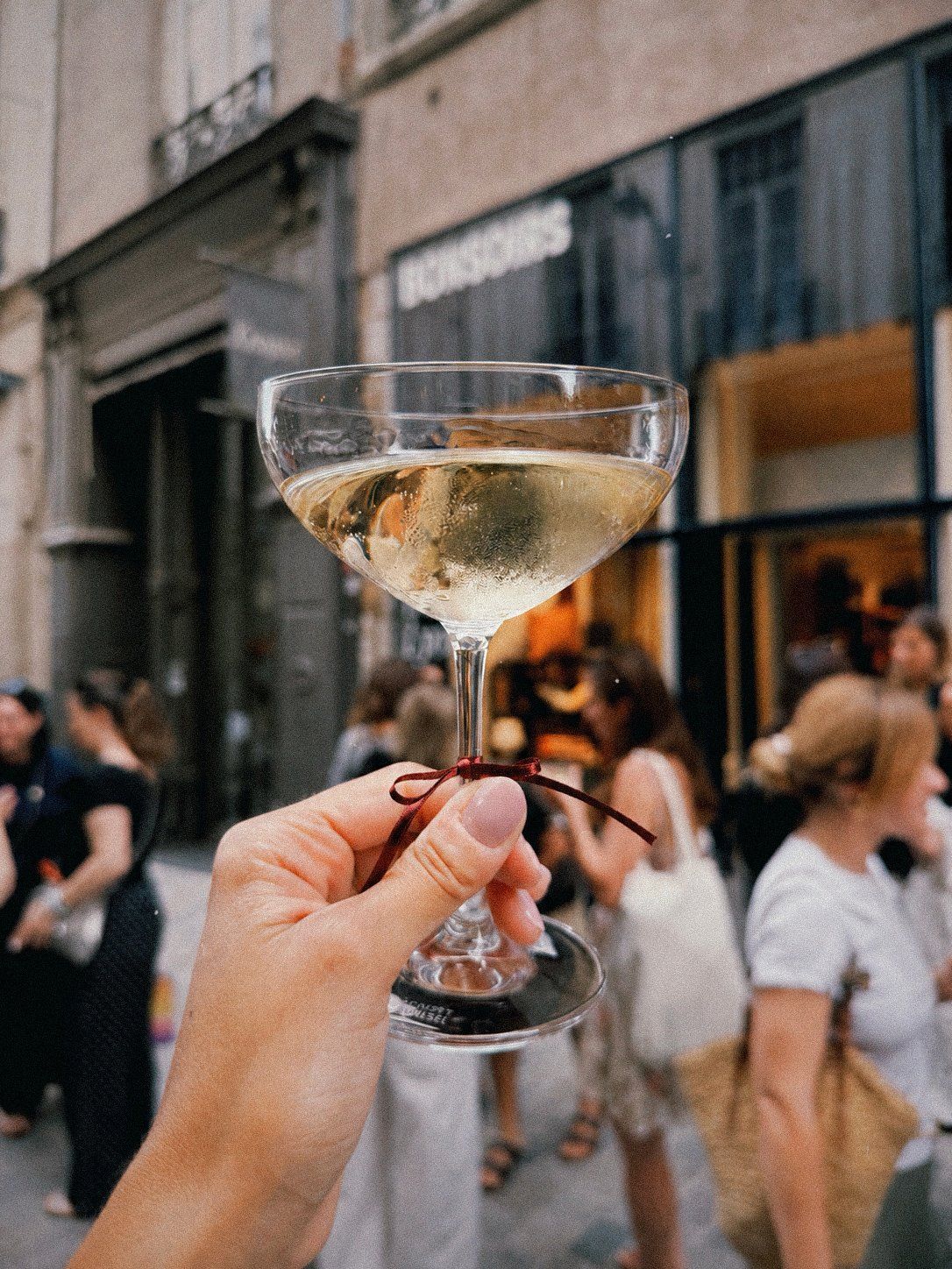 Coupe de champagne nouée d'un ruban, levée lors d'un événement en terrasse dans une rue de Lyon